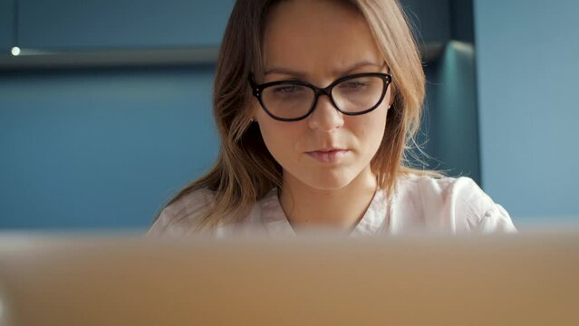 Young woman lady face with stylish black hipster glasses. You can see girl eyes moving, blinking while she is reading text or looking at laptop computer. Her face is calm and attitude serious, focused