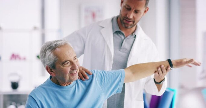 Physiotherapist stretching a senior man with shoulder pain and massaging his arm in a clinic to help him. A male chiropractor doing a treatment on a mature or old guy by doing an exercise