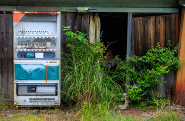 Old broken vending machine in front of abandoned shop with overgrown weeds