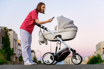 Obraz premium A young mother walks with her child around the city in a stroller. A woman in a pink T-shirt walks with her newborn baby in the city