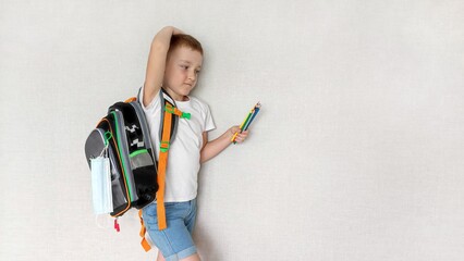Back to school. Boy with a backpack getting ready for school, light background and copy space, the concept of preparing for school, primary school student shows fatigue