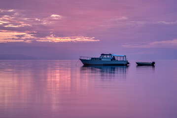 motor boat with dinghy lying at anchor in the pink mirror gloss sunrise