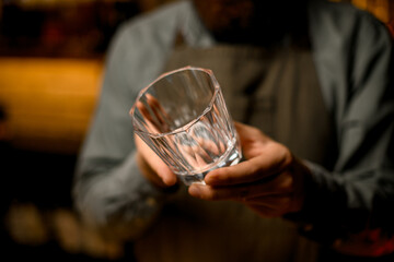 Selective focus on empty glass for drink in male bartender hands. Blurred background