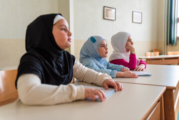 Group of children Muslim girls in hijab sitting at the school desk in the classroom during the class.