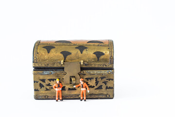 Miniature worker in safety suit with wooden treasure box isolate on white background, jewellery box security adn asset insurance concept