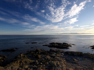 Fototapeta na wymiar rocky beach with small peninsula or islet and blue skies and clouds