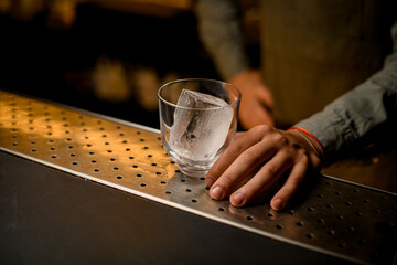 close-up of glass with ice cube on bar and male hand near it