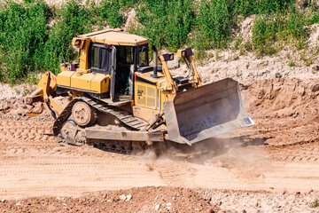 A powerful bulldozer in a sand pit is planning a site. Extraction of sand in an open pit. natural building materials.