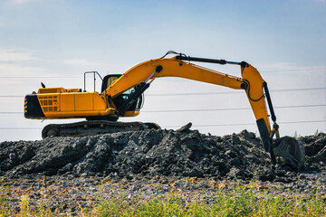 A powerful caterpillar excavator digs the ground against the blue sky. Earthworks with heavy...