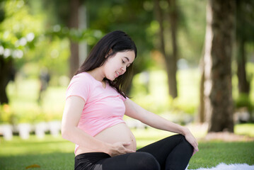 Asian happy pregnant woman in the garden and touching her belly. pregnancy, motherhood, people and expectation concept