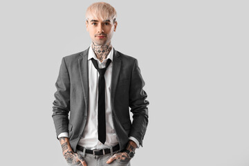 Young tattooed man in suit on light background