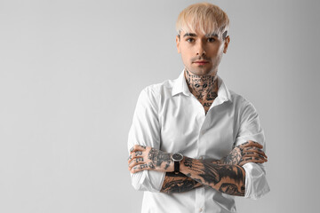 Young tattooed man in white shirt on light background