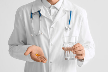 Young doctor with pills and glass of water on white background
