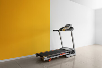 Modern treadmill near yellow and white wall