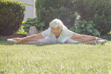 an aged elderly gray-haired woman does therapeutic exercises for stretching muscles and hip joints. exercise splits, yoga asana. High quality photo