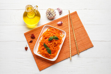 Plate with carrot salad, chopsticks and ingredients on white wooden background