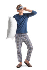 Young man with sleeping mask and pillow on white background