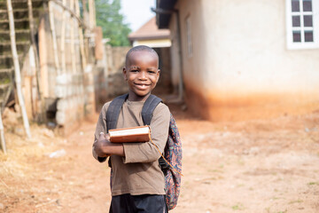 Fototapeta premium An African boy student wearing bag pack and holding school books smiling and looking at camera