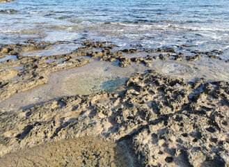 The coast of the Mediterranean Sea, long frozen lava, in the recesses of which water splashes.