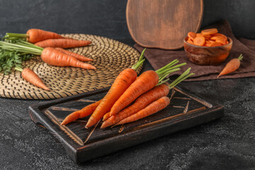 Wooden board with fresh carrots on dark background