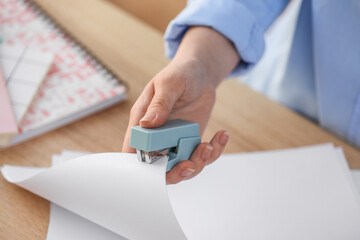 Woman with blue stapler and paper sheets at table, closeup - obrazy, fototapety, plakaty