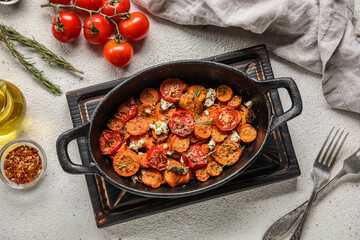Wooden board with baking dish of tasty baked vegetables on light background