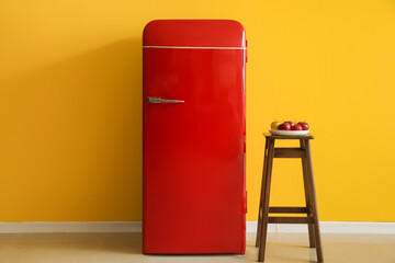 Plate with apples on stool and red fridge near yellow wall