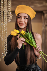 Beautiful stylish brunette woman with makeup in a yellow beret with yellow tulips indoors