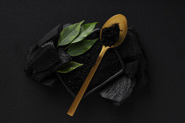 Charcoal, powdered charcoal, spoon and leaves on black background
