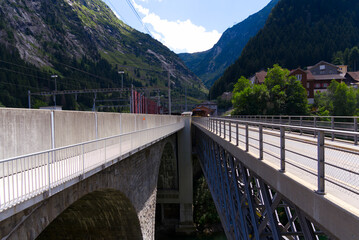 Stone railway bridge and metal car bridge over Reuss River at mountain village Göschenen on a sunny summer day. Photo taken July 3rd, 2022, Göschenen, Switzerland.