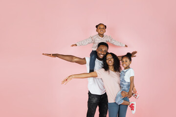 Family bonding concept. Joyful black man and woman holding daughters on hands, having fun over pink...