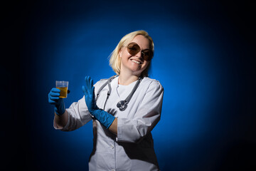 Funny female doctor in a white coat, gloves and glasses is disgusted by urine in a jar on a dark...