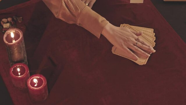 From above slowmo of unrecognizable fortune teller spreading out pack of tarot cards on red velvet cloth