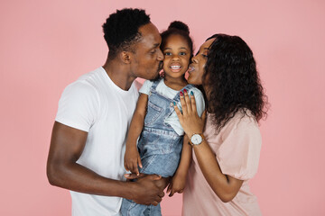 Happy african american woman and her husband kissing their daughter on pink background, everybody hugging together, free copy space, banner.