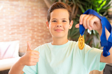 Cute child boy showing his gold medal with thumb up standing on the terrace at home, outdoors.