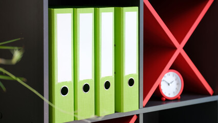 Shelves with office folders with documents and red alarm-clock
