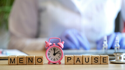 Word menopause made of wooden blocks in raw and pink alarm-clock