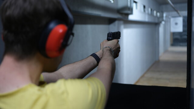 Male shooter in headphones aiming pistol at target in shooting range