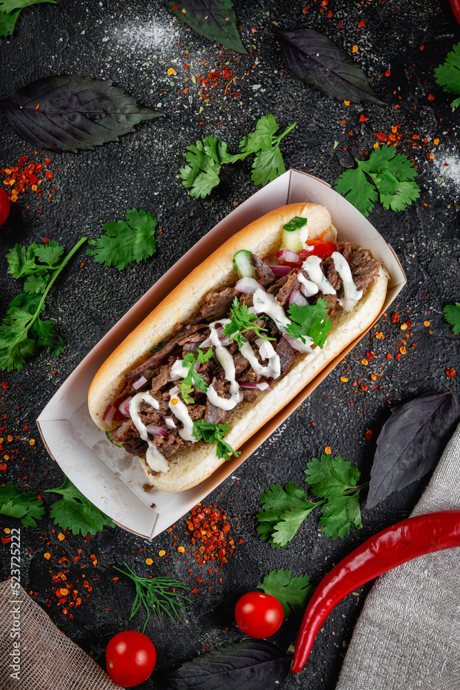 Wall mural Hot dog with vegetables, stuffing with chicken, beef and herbs on a dark stone table. The concept of fast food and delivery restaurants