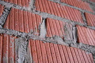 Fragment of brickwork half in the shade. Flat lay, close-up. Cracks and flaws in the red brick on the wall are illuminated by bright light from one side.