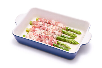 ceramic baking dish with aspargus covered with bacon isolated on white background