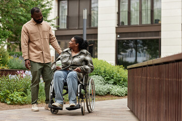 Full length portrait of happy black couple with young woman in wheelchair enjoying walk in city...