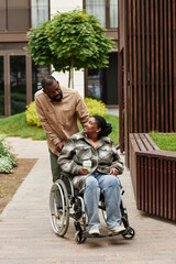 Vertical full length portrait of black couple with young woman in wheelchair enjoying walk in city...