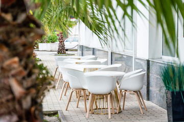 Street cafe with white chairs, green foliage around. Without people, tourism, travel.