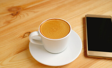 A Cup of Hot Coffee with Blank Screen Smartphone on Wooden Table