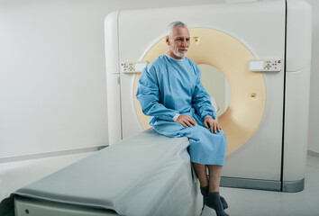 Old man having CT scan procedure sitting on CT machine scanner in radiology department of hospital