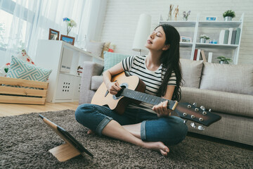 dutch angle asian musician sitting crossed legged on living room floor with closing eyes is...