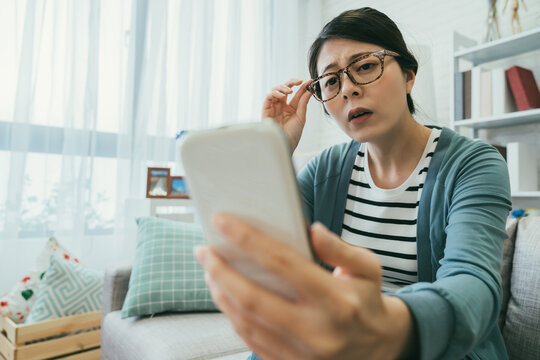 selective focus asian woman having presbyopia is holding her glasses and squinting her eyes while trying to read clearly on the phone at a home living room