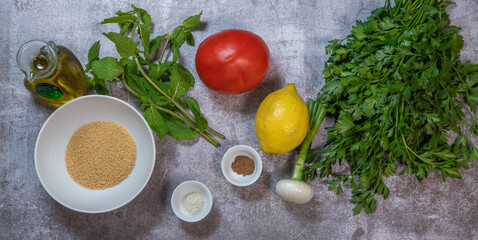 Ingredients for one Parsley salad or Tabbouleh, easy and healthy classic vegetarian dish with bulgur, tomatoes, parsley, spring onion and mint, olive oil on grey background, High quality photo
