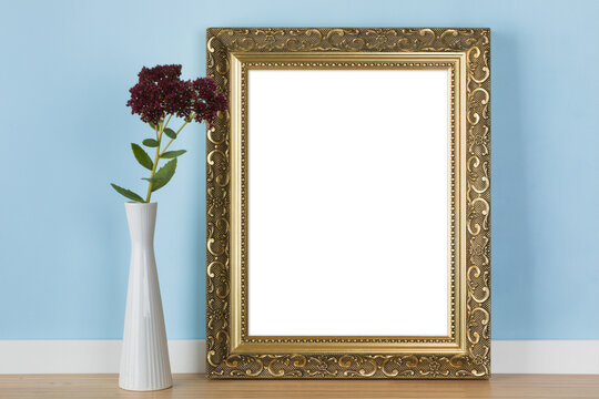 Vertical golden picture frame leaning on blue wall with stonecrop flowers in vase transparent mockup template